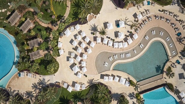 An aerial view of a resort with a large pool, sun loungers, and palm trees. - City of Dreams Mediterranean (Limassol)