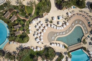 An aerial view of a resort with a large pool, sun loungers, and palm trees. - City of Dreams Mediterranean (Limassol)