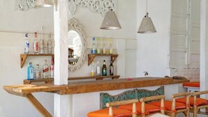 A bar area with wooden shelves holding bottles, a mirror, and hanging lamps.