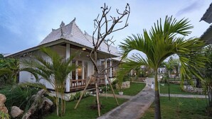 A traditional-style building with a tiled roof, surrounded by a well-maintained garden with palm trees and a concrete pathway.