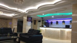 A lobby with a reception desk, two black leather sofas, a coffee table, and a chandelier. - Hotel Privilege (Bir El Djir)