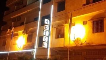 Un immeuble d’hôtel à plusieurs étages, doté d’une enseigne lumineuse et devant lequel est garée une voiture blanche.