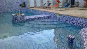 A swimming pool with tiled steps leading into the water, surrounded by lounge chairs and a building with multiple doors. - Hotel Privilege (Bir El Djir)