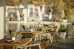 An outdoor dining area with wooden tables and chairs, potted plants, and clear glassware. - Once in Mykonos Luxury Resort - Designed for Adults (Mykonos)