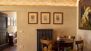 Un coin repas avec une table ronde, des chaises en bois et un radiateur. Des reproductions botaniques encadrées ornent le mur.