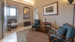 Un salon chaleureux avec un canapé, des fauteuils, une petite table ronde sur laquelle se trouve une bouteille, un miroir et un tableau encadré accroché au mur.