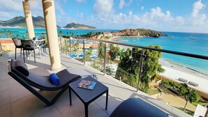 Un balcon avec un fauteuil de relaxation, une petite table et une vue sur une plage et l’océan.