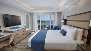 Une chambre d’hôtel avec un lit, un bureau, une télévision et une vue sur la mer.