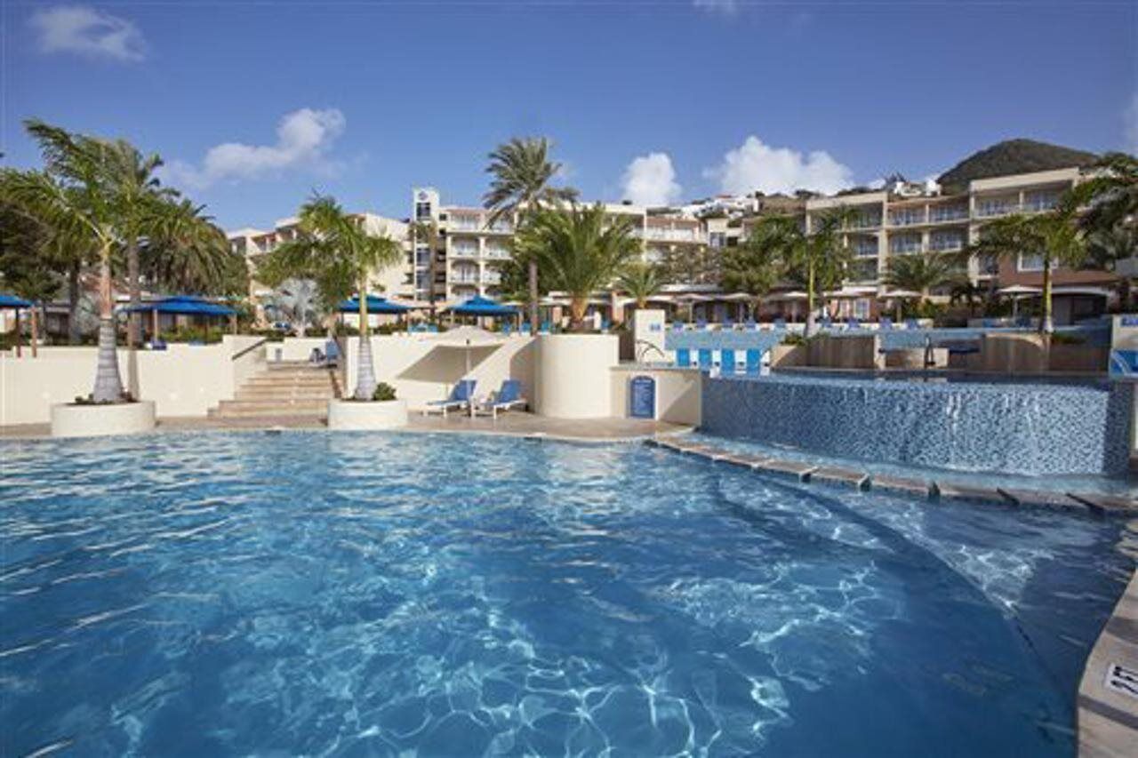 A swimming pool with lounge chairs and palm trees, surrounded by hotel buildings.
