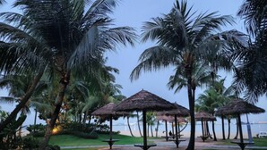 A beachside park with thatched umbrellas and palm trees. - Forest City Eco Stay (Gelang Patah)