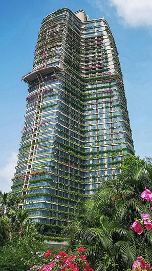 A high-rise building with multiple balconies, surrounded by lush greenery and flowering plants. - Forest City Eco Stay (Gelang Patah)