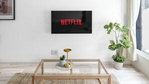 Ett modernt vardagsrum med en platt-TV som är monterad på väggen och visar "NETFLIX".