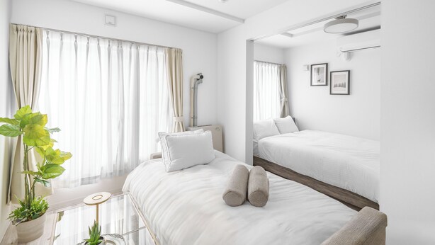 Ett modernt hotellrum med en stor säng, en mindre säng, en krukväxt och en spegel på väggen.