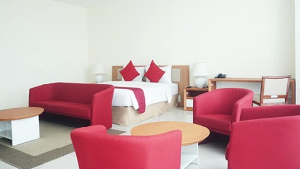 Una habitación de hotel moderna con una cama, sofás rojos, una mesita de madera y un pequeño escritorio de madera.