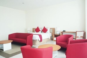 Une chambre d’hôtel moderne avec un lit, des canapés rouges, une table d’appoint en bois et un petit bureau en bois.