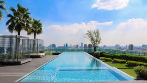 Piscina infinita en la azotea con vista al horizonte de la ciudad, rodeada de palmeras y follaje.