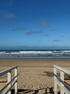 Une plage avec une promenade en bois menant à l’eau, des vagues qui déferlent et un ciel dégagé.