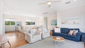 Un vaste espace de vie comprenant un canapé bleu, deux fauteuils, une table basse et un coin repas avec une cuisine en arrière-plan.