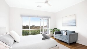 Une chambre à coucher avec un lit, un canapé gris, une grande fenêtre donnant sur un beau paysage et un ventilateur de plafond.