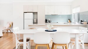 Une cuisine moderne avec des meubles blancs, un îlot central et un coin repas avec des chaises blanches.