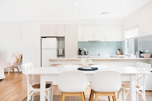 A modern kitchen with white cabinetry, a central island, and a dining area with white chairs. - Beach by the Dunes: Relaxing, contemporary beach house, walk to beach and river (Goolwa Beach)
