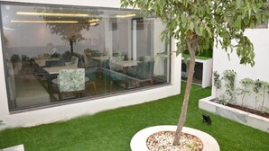 Un jardín interior moderno con pared de vidrio, césped artificial y maceta para un árbol.