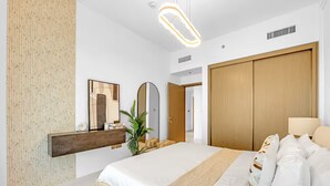 A modern hotel room with a large bed, a wooden wardrobe, a mirror, and a wall-mounted shelf. - Elegant 1BR at Emmar Beachfront (Dubai)