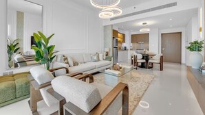A modern living room with a sofa, coffee table, and chairs. There is a kitchen area in the background. - Elegant 1BR at Emmar Beachfront (Dubai)
