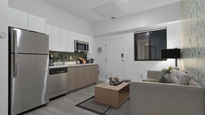Ett modernt kök med vitvaror i rostfritt stål, en mikrovågsugn och en diskmaskin. Det finns ett soffbord i trä och en soffa med kuddar.