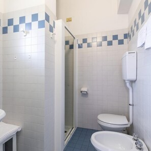 A bathroom with white tiles, a shower, a toilet, and a sink. - Hotel Sole (Cattolica)