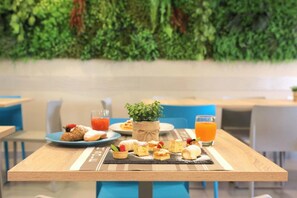 A dining table with a variety of pastries and a small plant, set against a backdrop of a green wall. - Hotel Sole (Cattolica)