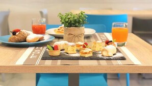 A table with pastries, a small plant, and drinks, set against a green wall. - Hotel Sole (Cattolica)