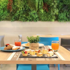A table with pastries, a small plant, and drinks, set against a green wall. - Hotel Sole (Cattolica)