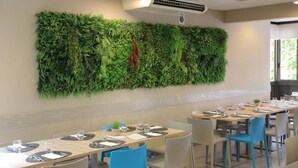 A dining area with tables set for meals, a wall-mounted air conditioning unit, and a large green vertical garden. - Hotel Sole (Cattolica)