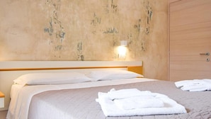 A bedroom with a bed, a nightstand, a wall-mounted light, and a wooden wardrobe. - Hotel Giulio Cesare (Cattolica)