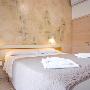 A bedroom with a bed, a nightstand, a wall-mounted light, and a wooden wardrobe. - Hotel Giulio Cesare (Cattolica)