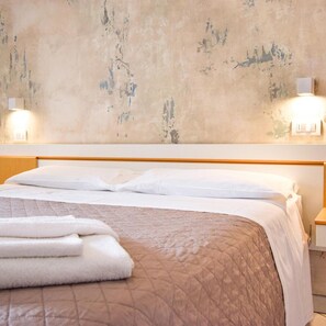 A bed with white linens, a brown quilt, and folded towels. There are two wall-mounted light fixtures on either side of the bed. - Hotel Giulio Cesare (Cattolica)