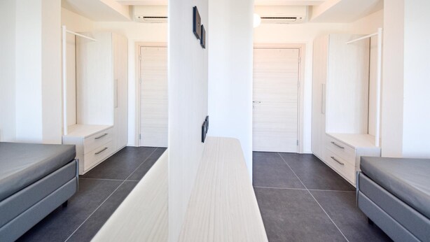 Een moderne hotelkamer met een centraal geplaatst bed, twee nachtkastjes, een grote spiegel en een kledingkast.