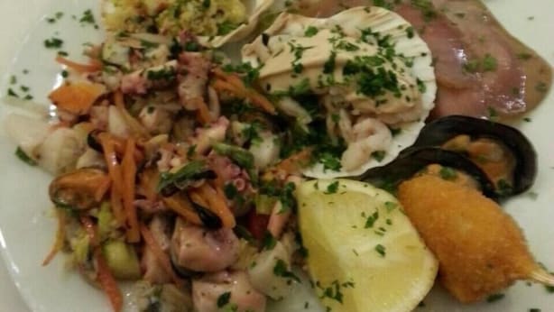 A plate of food with various items including seafood, a lemon wedge, and a breaded item. - Hotel Giulio Cesare (Cattolica)