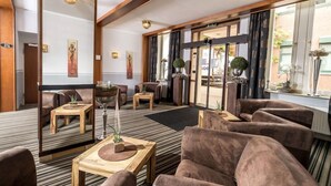 Un vestíbulo de hotel con diseño moderno, que cuenta con sofás de cuero, mesas de madera y amplias ventanas con cortinas.