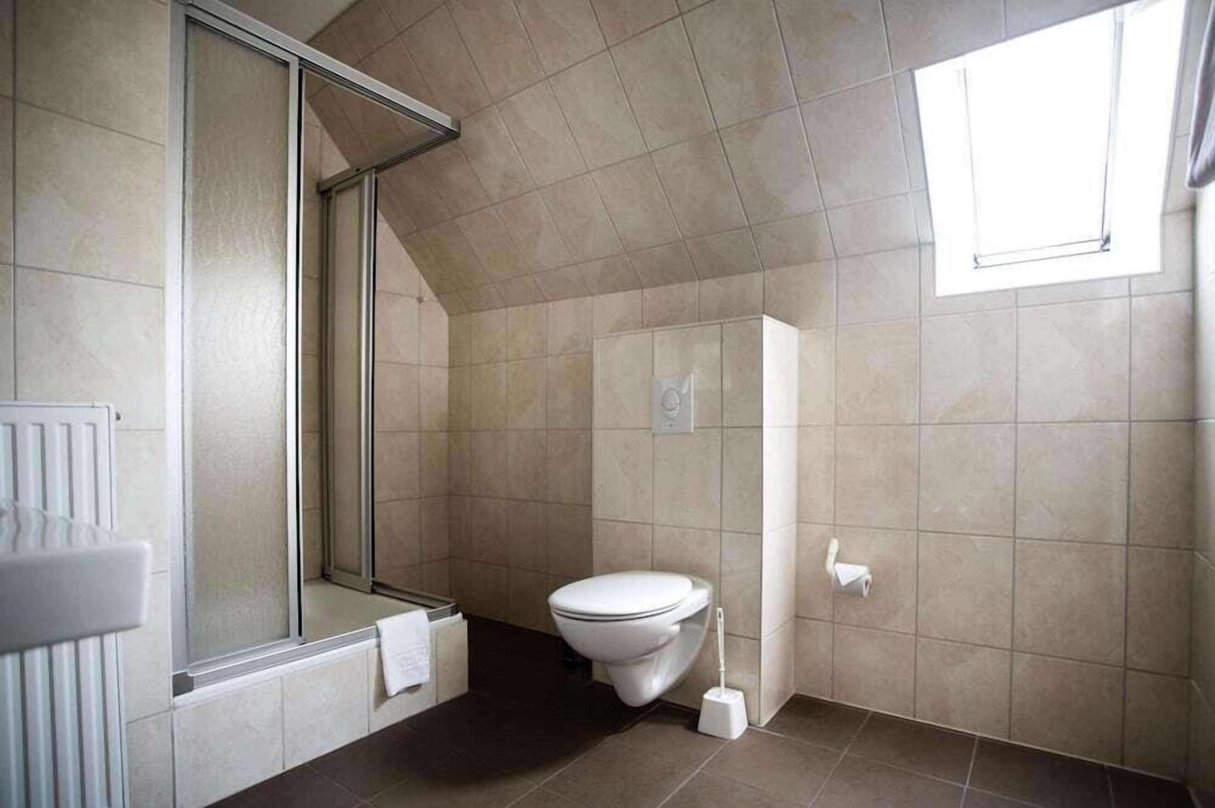 A modern bathroom with a shower, toilet, and a window providing natural light.
