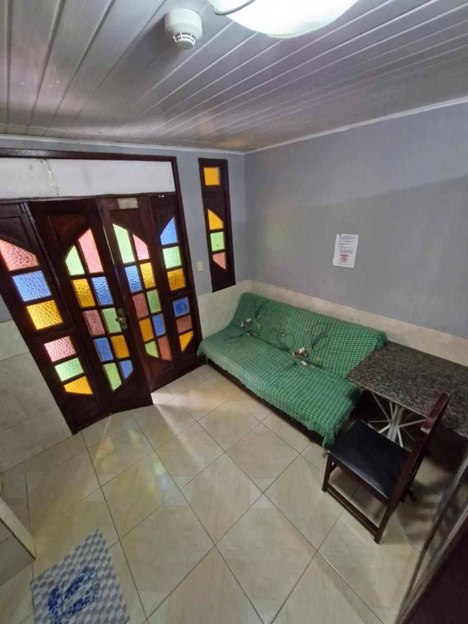 Quarto com um sofá verde, uma mesinha e uma porta com painéis de vitrais coloridos.