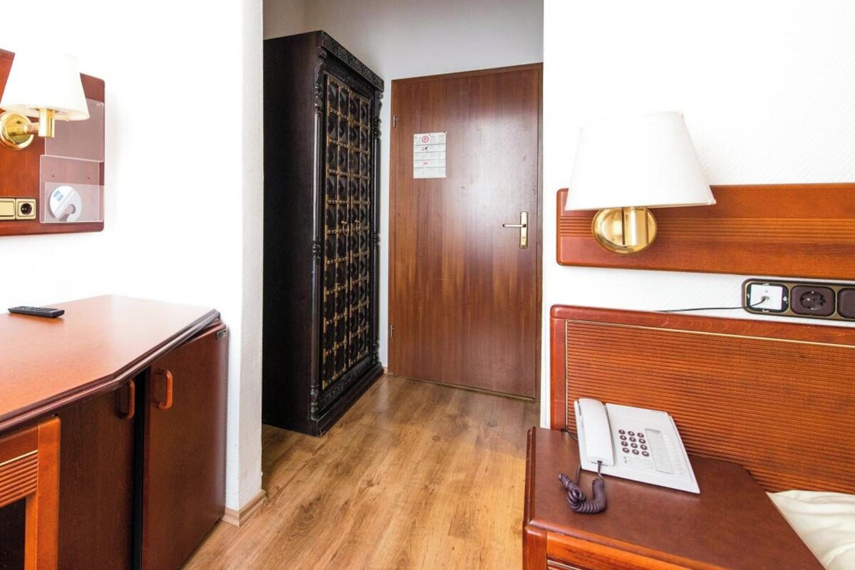Habitación de hotel con escritorio de madera, teléfono, lámpara y puerta que da a un pasillo.