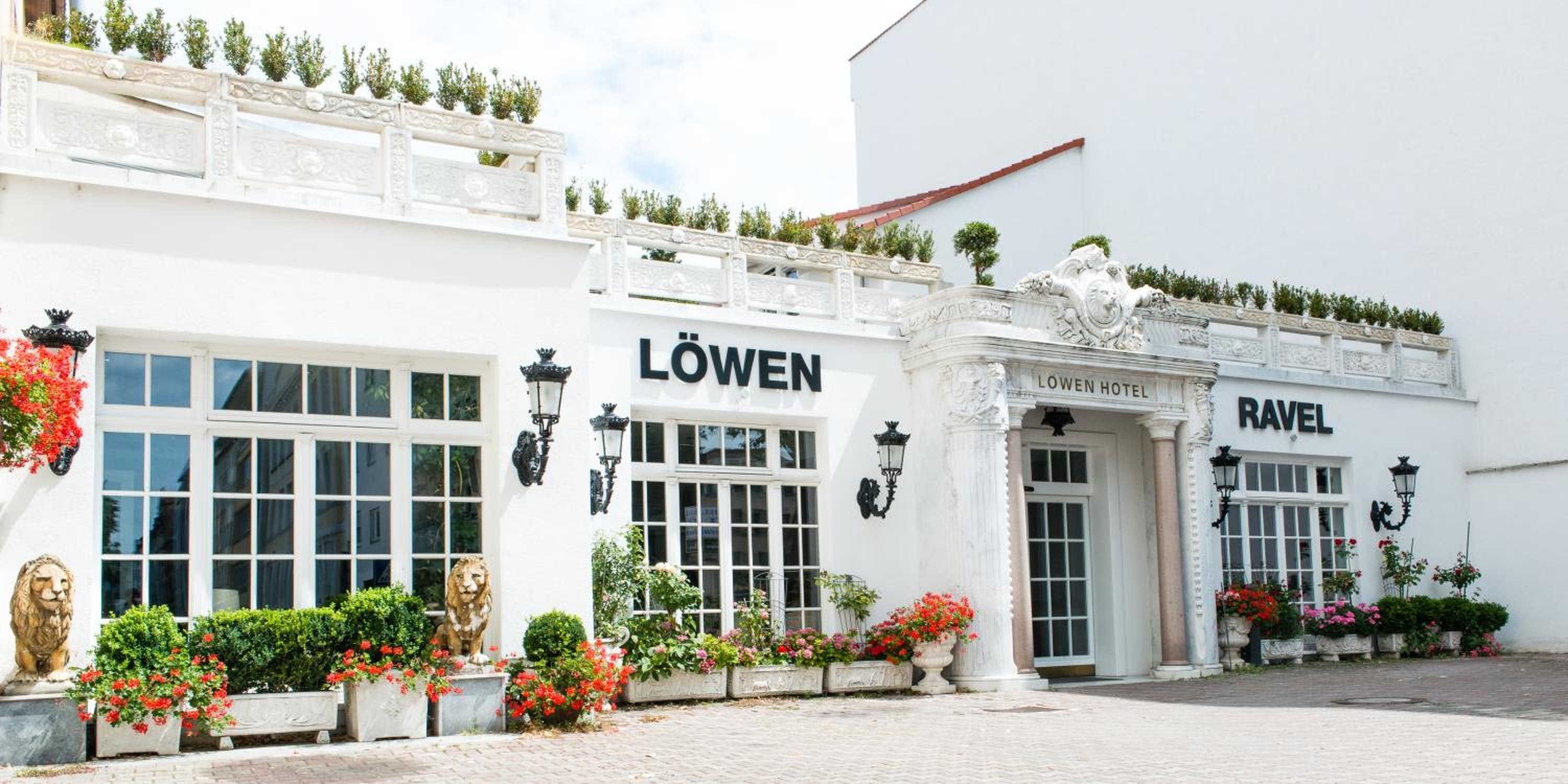 Ein Hotel mit heller Fassade, großen Fenstern und einem Schild, auf dem 'LÖWEN HOTEL' steht.