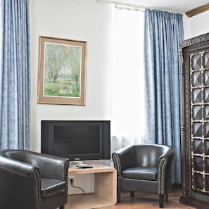 A room with a television, two leather chairs, a desk, and a framed painting on the wall. - Lowen Hotel (Offenbach am Main)