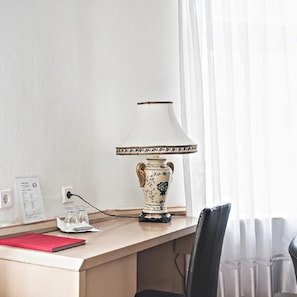 Un escritorio con una lámpara, una silla, una carpeta roja y un vaso.