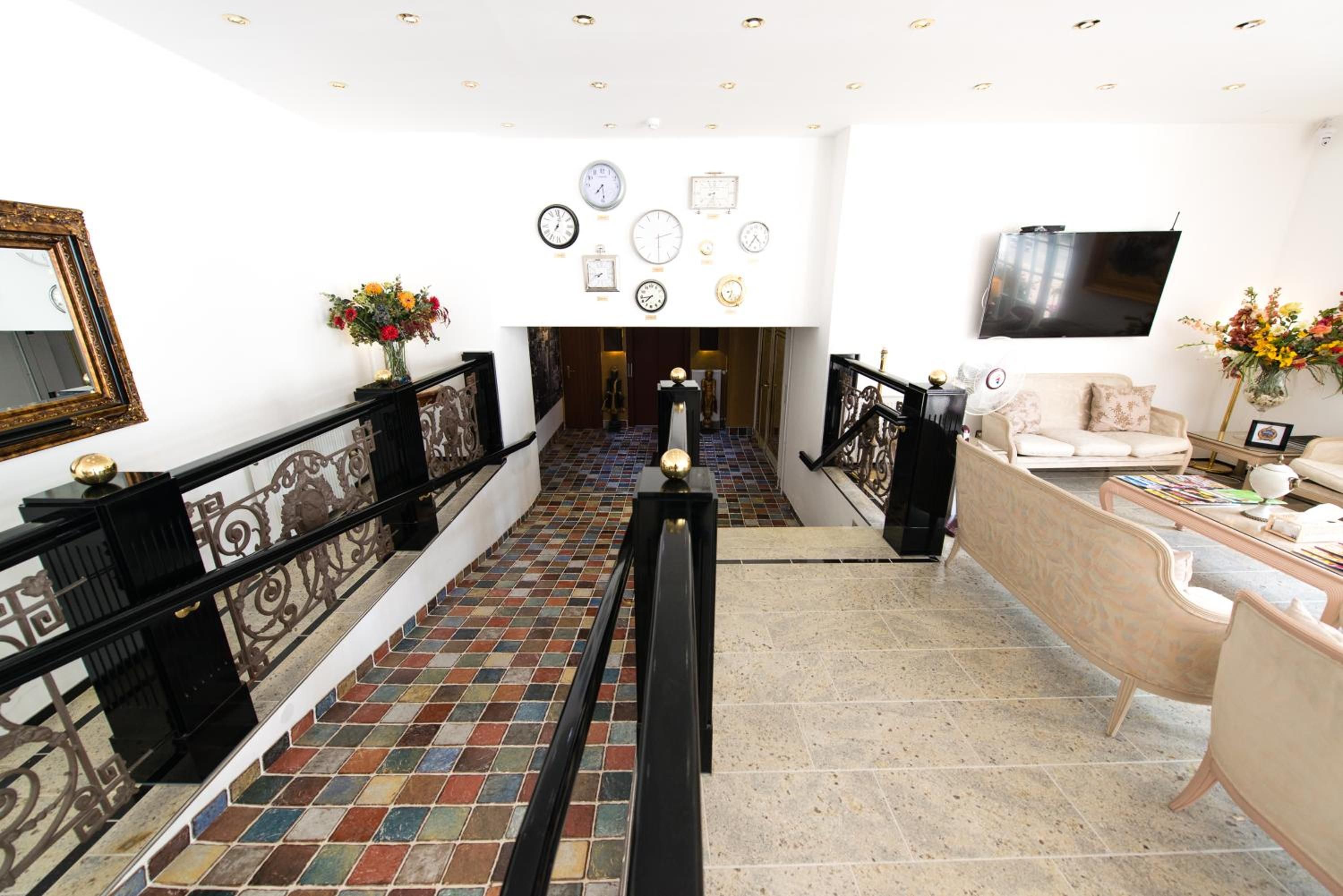 Eine Hotelhalle mit Treppe, einer Rezeption und einer Wand mit Uhren.