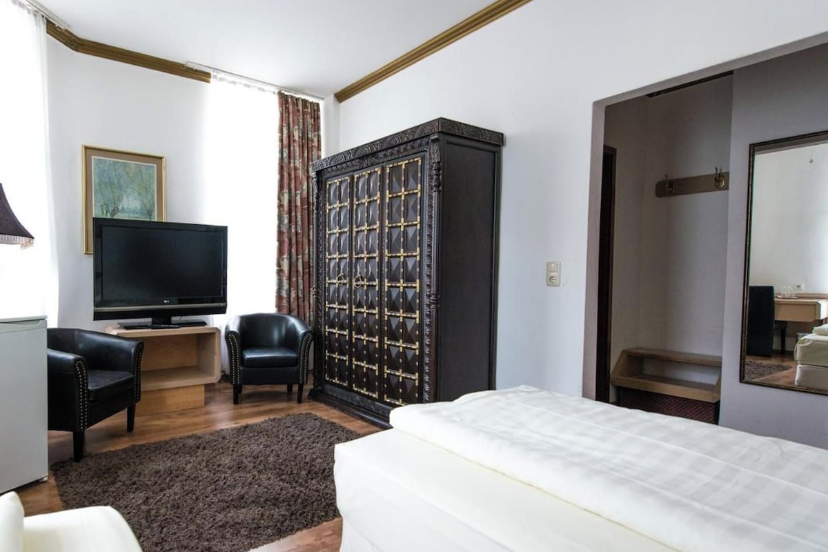 Habitación de hotel con cama, televisor, armario, escritorio y una silla.