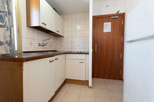 A kitchen with white cabinets, a wooden countertop, a stainless steel faucet, and a wooden door with a sign. - Rentalmar Blue Beach Apartments (Salou)