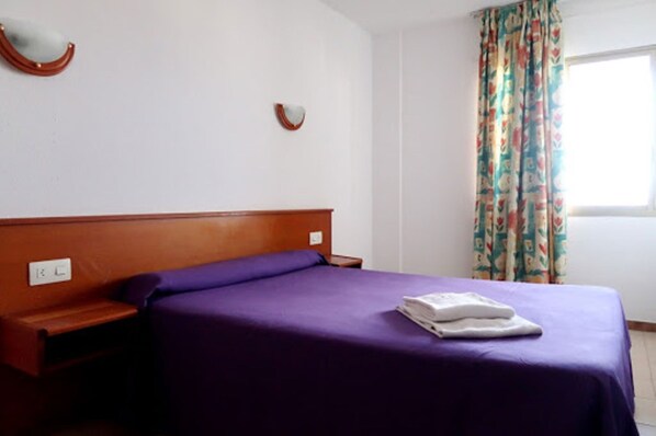 A single bed with a wooden headboard, a purple bedspread, and a folded white towel on the bed. - Rentalmar Blue Beach Apartments (Salou)